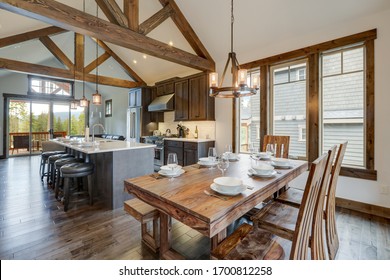 Amazing dining room near modern and rustic luxury kitchen with vaulted ceiling and wooden beams, long island with white quarts countertop and dark wood cabinets. - Shutterstock ID 1700812258