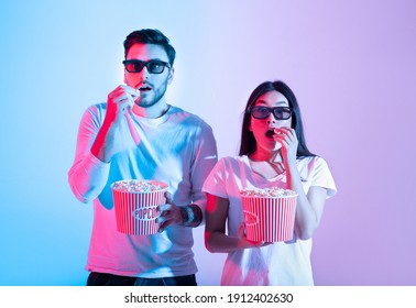 Amazing Entertainment, Leisure Time Together And Cinema With Modern Technology. Surprised Calm Young Guy And Lady In 3d Glasses Eating Popcorn And Watching Movie, In Neon, Studio Shot, Free Space