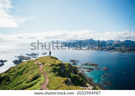 Amazing epic shot of young man hiker stand on top of mountain after long difficult hike in Lofoten Islands in Norway. Incredible summer views of scandinavian travel lifestyle. Epic landscape in north