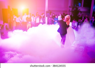 Amazing first wedding dance of newlyweds on low pink light and heavy smoke.  Photo with noise