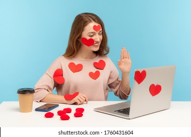 Amazing friendly woman with kind expression sitting all covered with sticker love hearts and gesturing hello talking on video call, romantic relationship on internet. indoor studio shot, isolated - Powered by Shutterstock