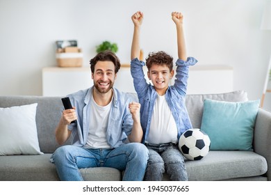 Amazing game. Overjoyed dad and son cheering football at home, emotionally supporting favorite team and celebrating goal with raised hands. Family watching sports on TV, sitting on sofa at home - Powered by Shutterstock