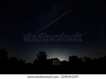 Amazing green and pink meteor trail streaking across night sky over a house in rural area 