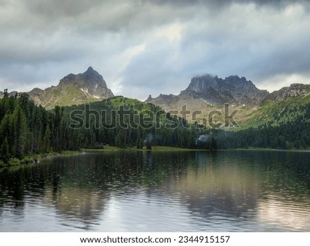 Amazing huge cloud above giant mountains. Raindrops on mountain lake. Wonderful droplets on lake water. Low clouds. Cloudy sky. Wonderful atmospheric ghostly highland landscape. West Sayans. 