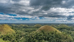 Amazing Karst Rounded Hills Covered With Brownish Grass Stretched To The Horizon. Tropical Vegetation All Around. Clouds In The Blue Sky. Chocolate Hills Natural Monument. Philippines. Bohol.