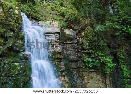 Amazing landscape of beautiful waterfall on mountain river with white foamy water falling down from rocky cliff in summer rainforest.