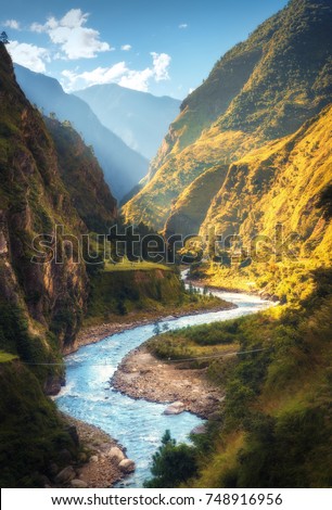 Amazing landscape with high Himalayan mountains, beautiful curving river, green forest, blue sky with clouds and yellow sunlight in autumn in Nepal. Mountain valley. Travel in Himalayas. Nature