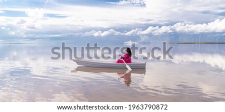 Amazing landscape lake white clouds and mixed race woman in white boat pink fancy suit sitting with closed eyes holding paddle oar. artistic dreams subconscious representation. Long horizontal banner 