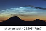 Amazing magical silver noctilucent clouds or night shining clouds NLCs above Czech Central Mountains silhouette