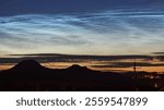 Amazing magical silver noctilucent clouds or night shining clouds NLCs above Czech Central Mountains silhouette