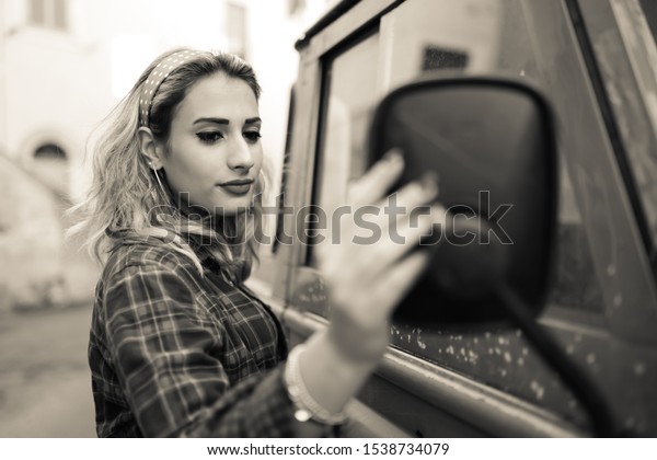 Amazing model\'s portrait, black and white\
photo. Attractive girl looking sadly in the mirror of the car.\
Fashion model and\
transportation