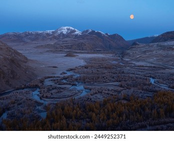 Amazing mystical moonlit night in a mountain valley. Winding river at dusk. Big moon over a snowy mountain. Golden full moon rising over distant mountains in the blue hour. Perfect image for wall - Powered by Shutterstock