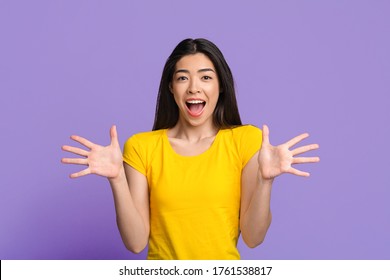 Amazing Offer. Surprised asian woman with opened mouth spreading arms with excitement, looking at camera over purple studio background, copy space