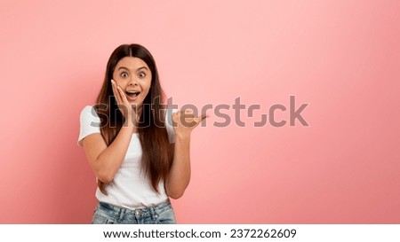 Amazing Offer. Surprised Teen Girl Pointing Aside With Her Thumb Up, Emotional Female Teenager Touching Face In Shock, Demonstrating Copy Space For Advertisement Design, Standing Over Pink Background