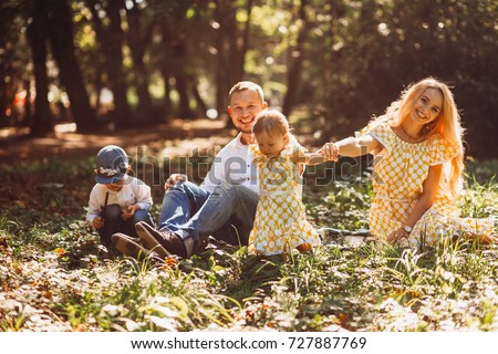 Amazing parents have fun with their two resting on a green lawn in park