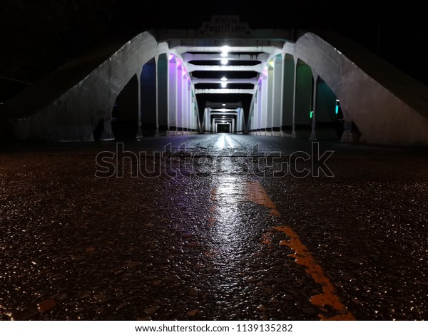 Amazing\
perspective and vanishing point with old white bridge at night, \
asphalt wet road surface, Ratchadapisek Bridge is the translation\
of thai writing on top bridge, Lampang,\
Thailand