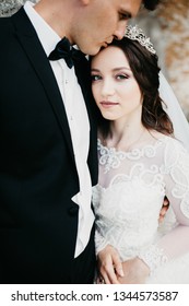 Amazing Picture Of A Wedding Couple Which Is Standing Near The Old Renaissance Palace. They Are Standing Face To Face, A Groom Kissing His Bride And She Is Looking At The Camera.