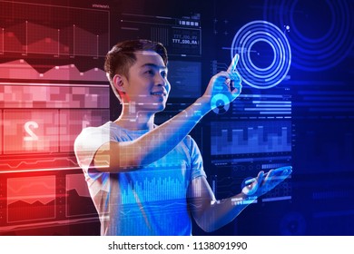 Amazing program. Cheerful enthusiastic web developer standing in his modern convenient office and smiling while touching a transparent screen