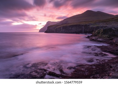 An amazing purple and mauve cloudscape sunrise lighting up the shoreline, nearby mountains and ocean water at Eidi in the Faroe Islands.
