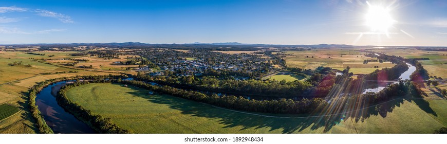 Amazing river bends among green fields and small town in Australian outback at sunset - wide aerial panorama