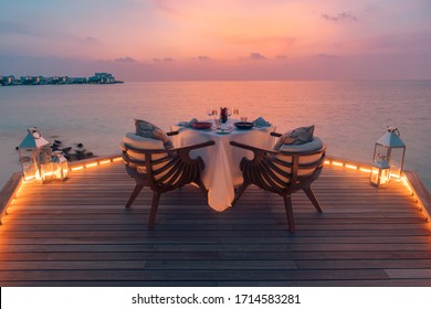Amazing romantic dinner on the beach on wooden deck with candles under sunset sky. Romance and love, luxury destination dinning, exotic table setup with sea view