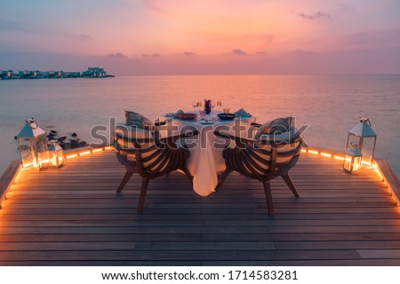 Amazing romantic dinner on the beach on wooden deck with candles under sunset sky. Romance and love, luxury destination dinning, exotic table setup with sea view