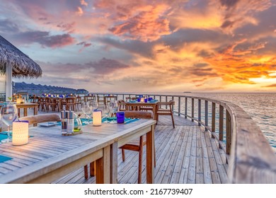 Amazing romantic dinner tables in outdoors beach restaurant. Wooden deck with candles under sunset sky. Vacation, honeymoon romance love, luxury destination dinning, exotic table setup with sea view
