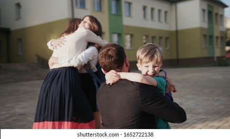 Amazing scene of happy family meeting together after work and school. Lovely parents higging and kissing their children in the school courtyard in sunny evening.