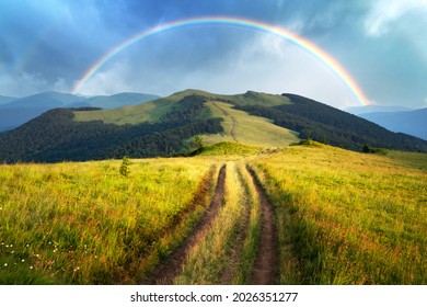 Amazing scene in summer mountains. Lush green grassy meadows in fantastic evening sunlight. Rural road and beautyful rainbow in dramatic sky. Landscape photography