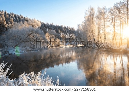 Amazing scenery of river and edge of forest in frosty morning. Ligth mist over river. Trees are reflected on the surface of the river as in the mirorr. Morning sunbeams red color on trees tops.