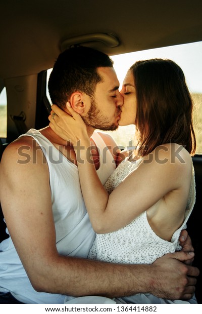 Amazing\
sexy caucasian couple kissing on the back bench of the car while\
resting near the road while traveling by\
car.