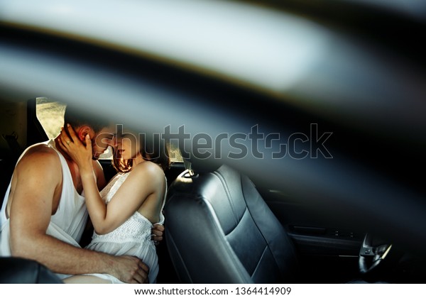 Amazing\
sexy caucasian couple kissing on the back bench of the car while\
resting near the road while traveling by\
car.