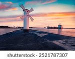 Amazing summer view of Stawa windmill with industrial cargo on background. Fantastic sunrise on Szczecin Lagoon. Nice morning seascape of Baltic Sea, Swinoujscie, Western Pomerania, Poland, Europe.