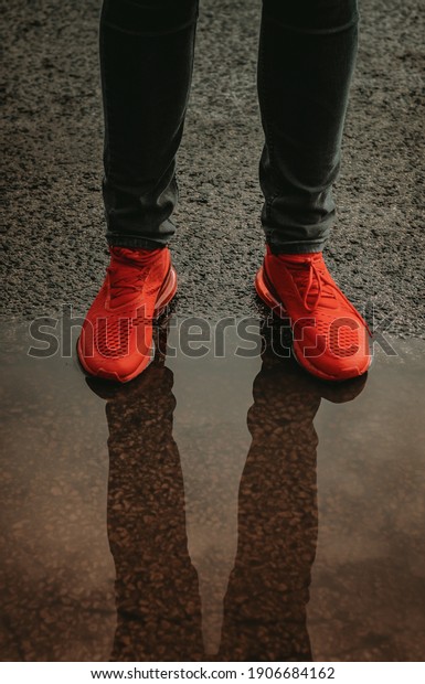 Amazing\
sunset image of red sports shoes reflecting in water. Men\'s\
sneakers reflect in rain water. Horizontally divided screen saver.\
Man wearing skinny jeans and fashion footwear\
