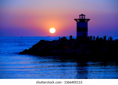 Amazing sunset on the beach with orange and blue tones reflecting on the sea water. Silhouet of fishing men and the lighthouse contrast with the colorful background. Scheveningen, Hague, Netherlands