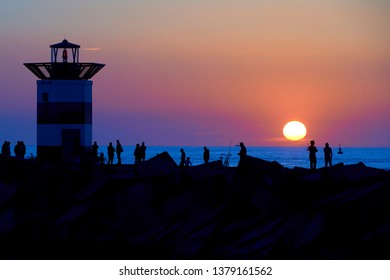 Amazing sunset on the beach with orange and blue tones reflecting on the sea water. Silhouet of people and the lighthouse contrast with the colorful background. Scheveningen, Hague, Netherlands