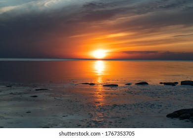 Amazing sunset on the Kabli Beach in Estonia. Darker looking image. Calm water during sunset last's moments. Beach full of stones and bushes. Golden hour ending, blue hour starting