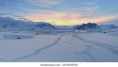 Amazing sunset over snowy Antarctic landscape. Snow covered frozen polar ocean and mountain range under colorful sunrise sky. Arctic winter nature. Antarctica travel and exploration. Aerial drone shot - Powered by Shutterstock