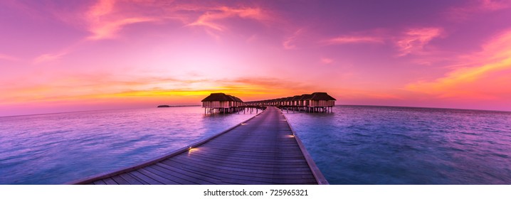 Amazing sunset panorama at Maldives. Luxury resort villas seascape with soft led lights under colorful sky.