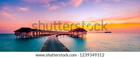 Amazing sunset panorama at Maldives. Luxury resort villas seascape with soft led lights under colorful sky. Beautiful twilight sky and colorful clouds. Beautiful beach background for vacation holiday