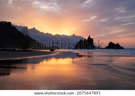 Amazing sunset with spectacular dramatic purple color sky reflecting into the water pools and the neat sand surface on the secluded Benijo beach or Playa de Benijo, in Tenerife, Canary Islands, Spain