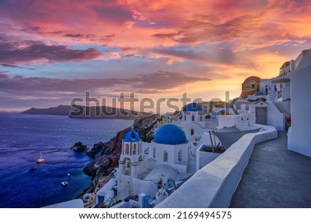 Amazing sunset view with white houses and blue domes in Oia village on Santorini island in Greece. Luxury summer travel destination, romantic sunset spot, amazing view over the caldera, sun rays cloud