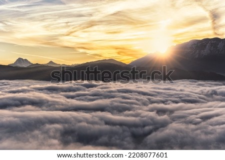 An amazing sunshine morning in Austrian Alps. The sun peaking from behind the mountain range and valley filled with thick fog. Amazing outdoor scene, adventurous. Terrific vacation destination.