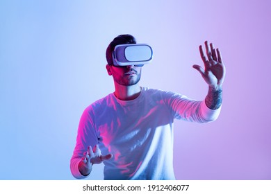 Amazing technology, online game, entertainment, study and virtual world in 3D simulation. Serious millennial man in vr glasses plays and tries to touch something, in neon, studio shot, free space