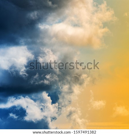 Amazing view of dramatic blue thunderclouds and stunning yellow-golden fluffy clouds illuminated by rays of sun. Natural meteorology background, cloudscape to weather change before rain.