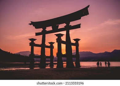 Amazing view of the great torii gate and group of travelers silhouettes, and sunset over the sea with mountains in the horizon, Japan