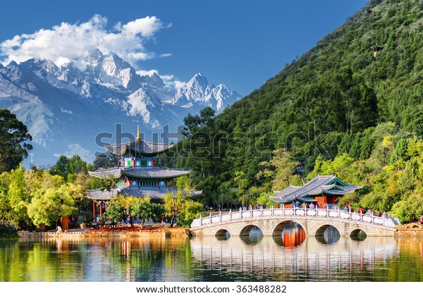 中國雲南省麗江市玉龍雪山和黑龍池的壯麗景色 玉泉公園內的水池上的壽嘴橋和月亮擁抱亭 庫存照片 立刻編輯