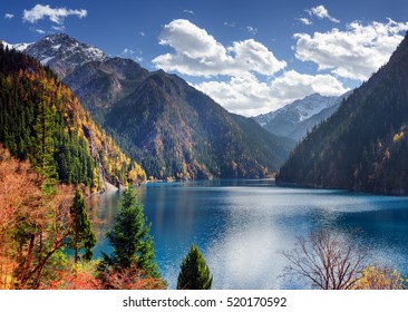 Amazing view of the Long Lake among colorful fall woods and snow-capped mountains in Jiuzhaigou nature reserve (Jiuzhai Valley National Park), China. Beautiful snowy peaks are visible in background.
