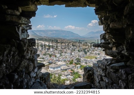 amazing view over Gjirokastra and the valley of the Drino River and the surrounding mountains through small window in the Gjirokastra fortress wall                              