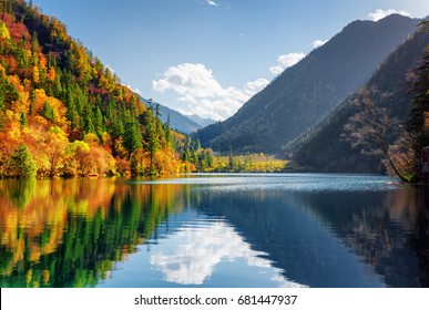 Amazing view of the Panda Lake among colorful fall forest at the Rize Valley in Jiuzhaigou nature reserve (Jiuzhai Valley National Park), China. Scenic wooded mountains and blue sky reflected in water